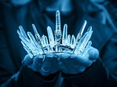 a person holding a crystal crown in their hands with blue lighting behind them and dark background