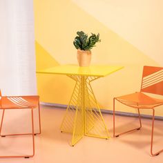 two chairs and a table with a potted plant on it in front of a yellow wall