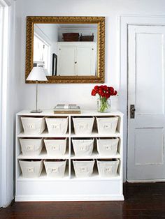 a white shelf with baskets and flowers in front of a large mirror on the wall