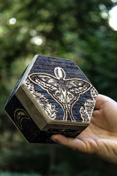 a hand holding an intricately carved wooden box in the palm of someone's hand