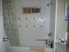 a bath tub sitting under a window next to a bathroom sink and toilet paper dispenser