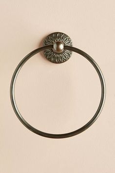 a metal towel ring with a pearl in the center on a beige wall behind it