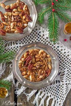 two glass bowls filled with nuts on top of a doily next to pine branches