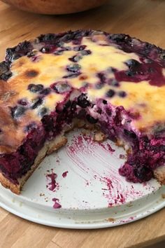 a blueberry cheesecake on a white plate with one slice missing from the pie