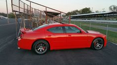 a red sports car parked in a parking lot next to a fence and grass field