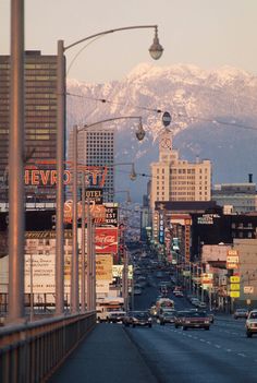 a city street filled with lots of traffic next to tall buildings and snow covered mountains