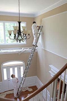 two men are painting the walls in a house with white paint and wood trimmings