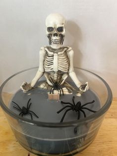 a skeleton sitting in a bowl with two black spider legs on the bottom of it