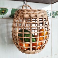 a wicker hanging basket filled with oranges and avocados on a tiled wall