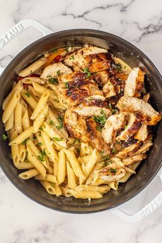 a pan filled with chicken and pasta on top of a marble countertop next to a knife