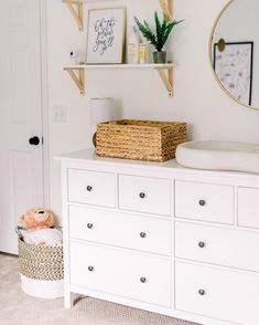 a baby's room with white dressers, shelves and a teddy bear in a basket