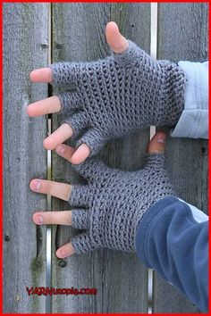 two hands wearing gray knitted gloves on top of a wooden fence