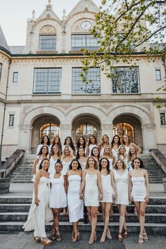 a group of women standing in front of a large building with stairs and windows on each side