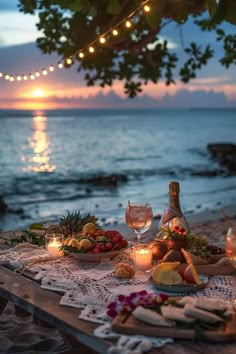 a table with food and wine on it near the ocean at sunset or sunrise time