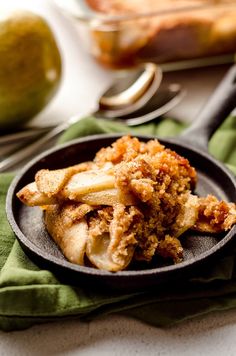 a skillet filled with food sitting on top of a green napkin next to an apple