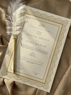 a wedding card with a feather on top of it next to a piece of paper