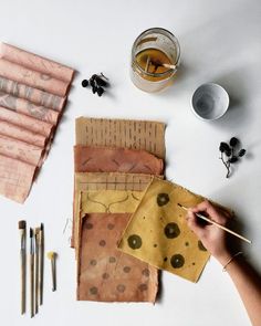 someone is painting fabric on the table with paintbrushes and other crafting supplies