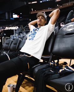 a young man sitting on top of a chair in front of a basketball court with his feet up