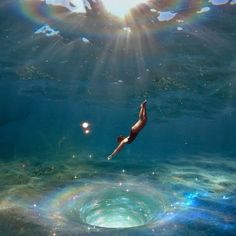 a woman swimming in the ocean with bubbles and sunbeams above her head as she dives into the water