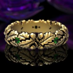 a gold ring with green stones and leaves on the front, sitting on a black surface