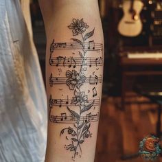 a woman's arm with music notes and flowers tattooed on the left inner forearm