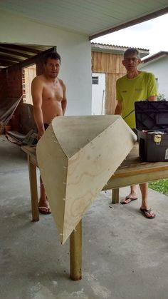 two men are standing next to a table with an object on it and one is holding a tool box