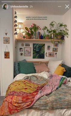 a bed with lots of pillows and blankets on it's headboard next to a shelf filled with plants