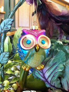 an owl ornament sitting on top of a green leafy plant next to a purple bird