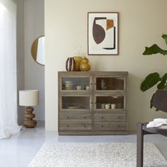 a living room with a chair, table and vases on top of the cabinet