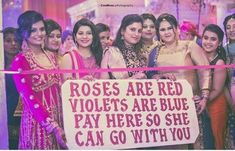 a group of women standing next to each other in front of a sign that says roses are red violets are blue pay here so she can go with you