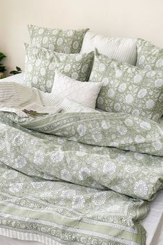 an unmade bed with green and white comforter, pillows and blankets on it