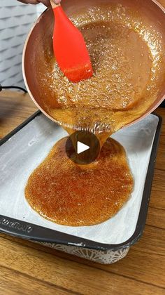 a person pouring something into a pan on top of a wooden table with a red spatula