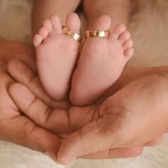 a person holding a baby's feet in the palm of their hand, with two gold rings on it