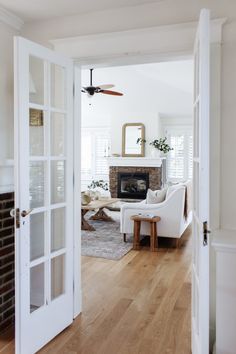 an open door leading to a living room with white furniture and a fireplace in the corner