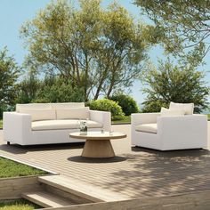 an outdoor living room with white furniture and trees in the background