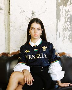 a woman sitting on top of a black leather couch next to a white brick wall