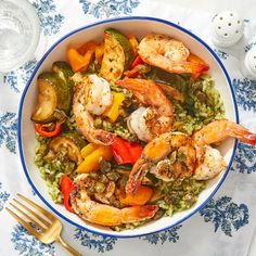 a bowl filled with shrimp and vegetables on top of a table next to utensils