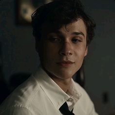 a young man in a white shirt and black tie looking at the camera with serious expression on his face