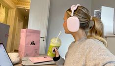 a woman sitting at a desk with headphones on and holding a drink in front of her