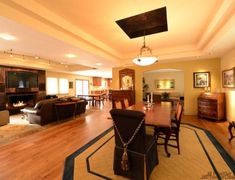 a large living room and dining area with wood flooring in the center is lit by recessed lights