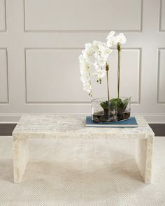 a white coffee table with flowers on top and a blue book sitting on the side