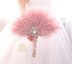 a woman in a white dress holding a pink feathered brooch with a diamond clasp