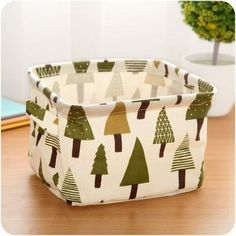 a white and green fabric basket with trees printed on the front, sitting on a wooden table