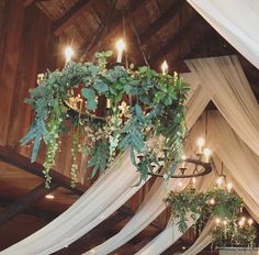 a chandelier with greenery hanging from it's ceiling in a barn