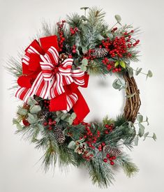 a christmas wreath with red and white bows, pine cones, evergreens, berries and holly