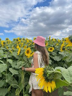 a girl in a pink hat is standing in a field of sunflowers and looking at the sky