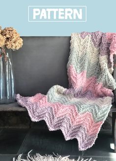 a crocheted blanket sitting on top of a bench next to a vase with flowers