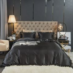 a bed with black sheets and pillows in a bedroom next to a white rug on the floor