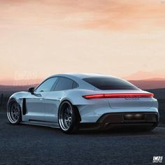 the rear end of a white sports car in front of a mountain range at sunset