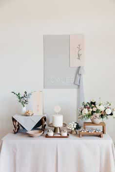 a table topped with cakes and flowers on top of a white table cloth covered table